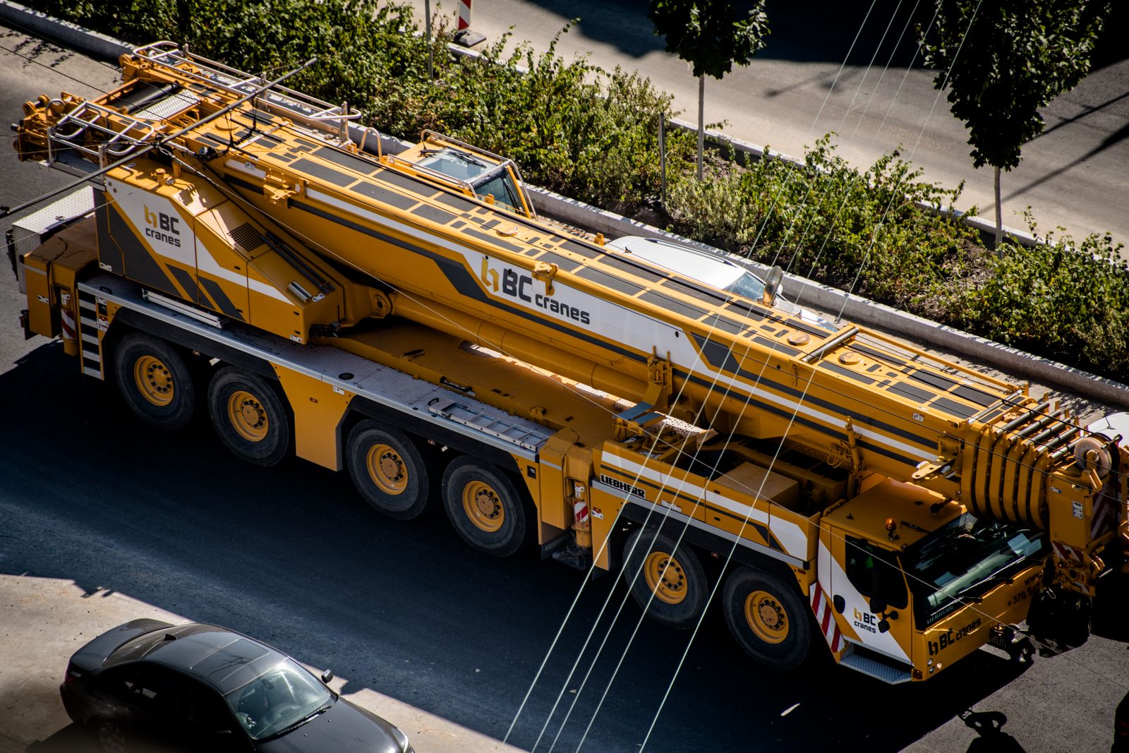 Overhead view of a yellow multi-axle all-terrain mobile crane with its boom stowed, parked on a city street