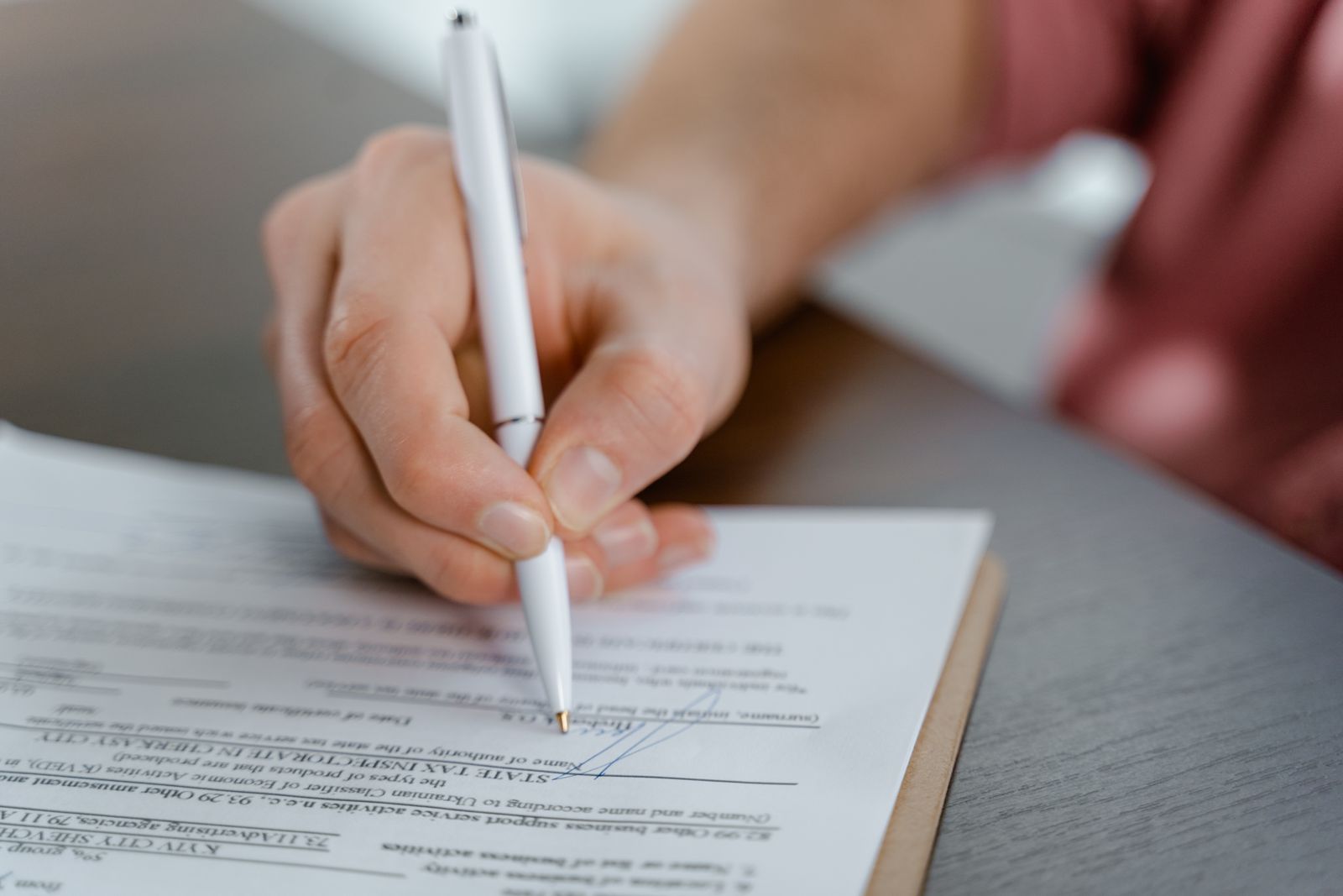 Close-up of a hand signing a printed form with a white pen on a desk